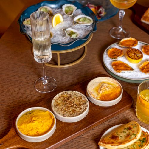 Assorted dishes and oysters on a table with drinks, bread, and dips arranged for a meal.