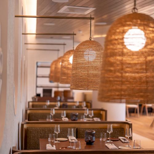 A cozy restaurant interior with woven hanging lamps, booths, and neatly set tables for dining, creating a warm, inviting atmosphere.